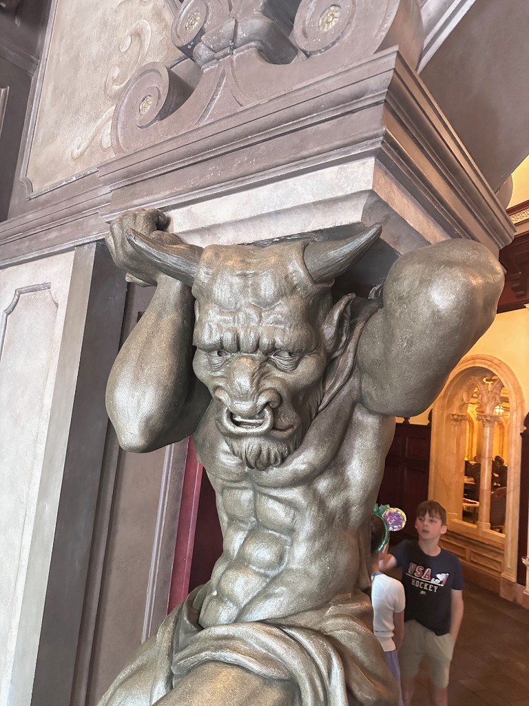 Gargoyle sculpture holding up a column inside Be Our Guest
