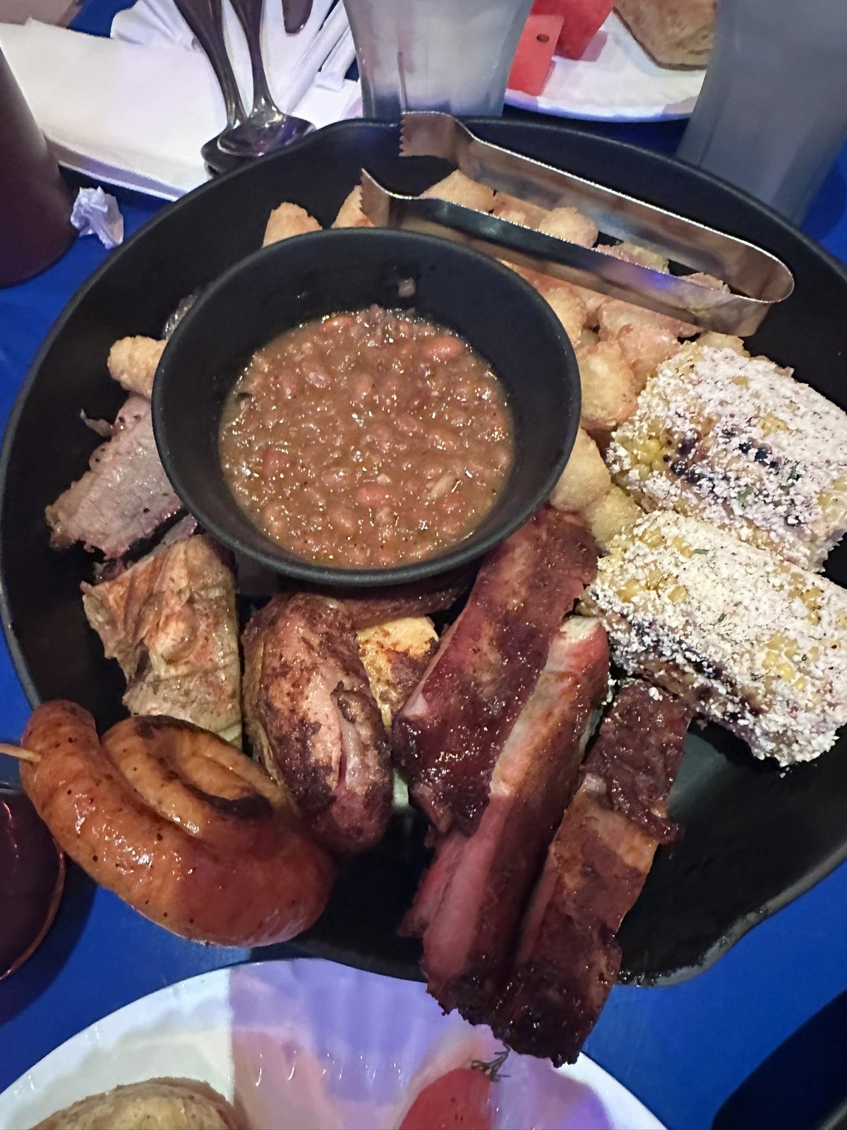 Family-style BBQ skillet with ribs, brisket, sausage, chicken, corn, and potato barrels