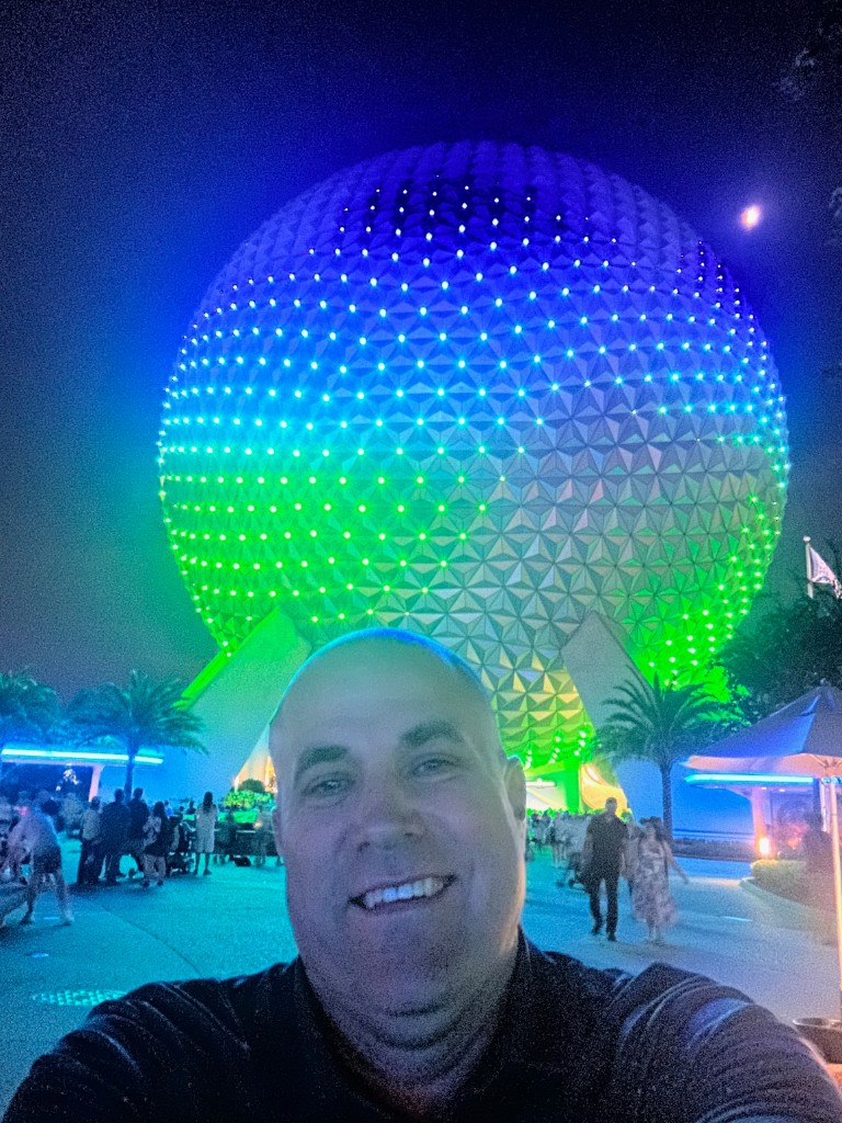 Ryan selfie with Spaceship Earth lit blue-green at night