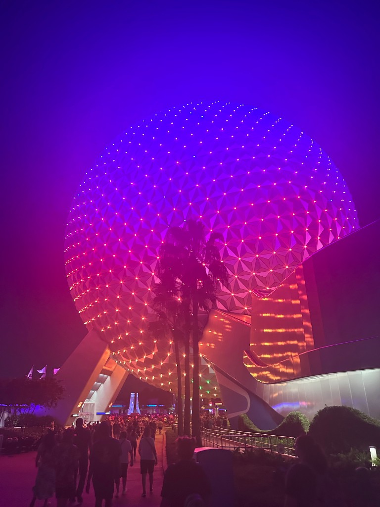 Spaceship Earth glowing purple and pink over a crowded exit