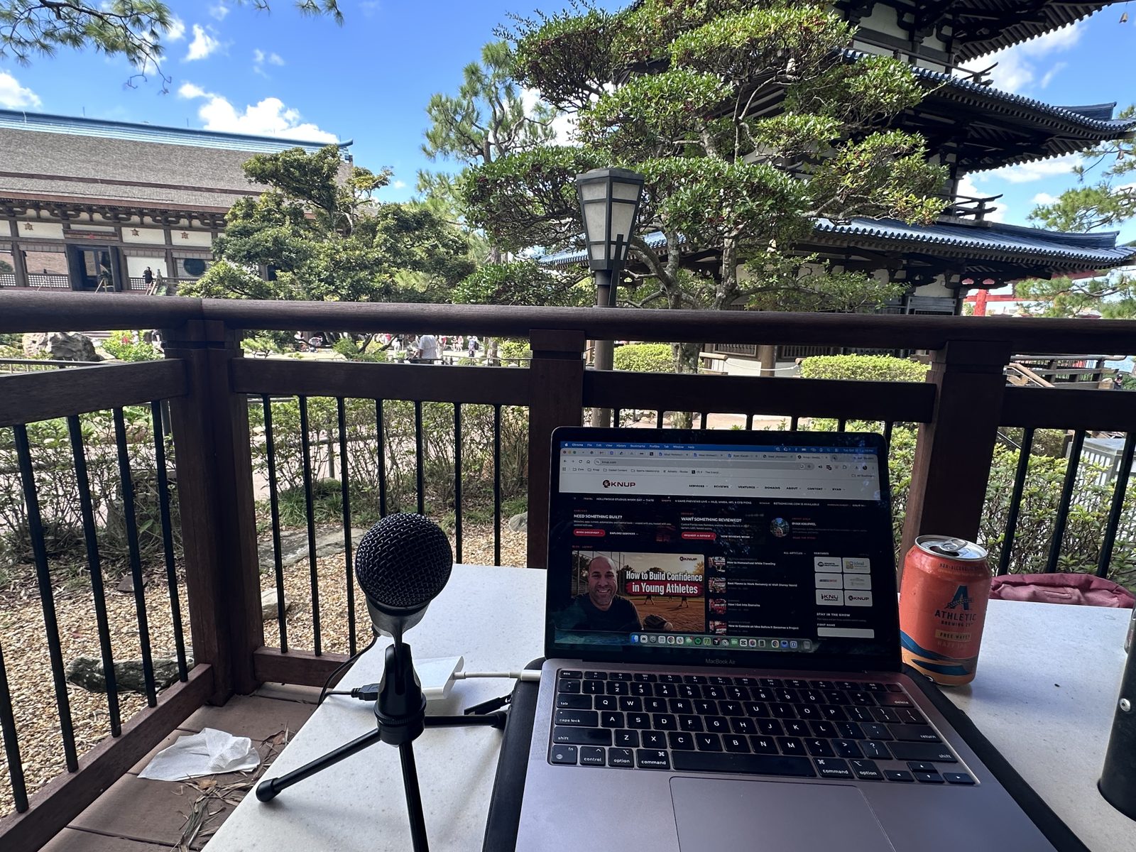 Laptop showing knup.com with a microphone and an Athletic Brewing can on a table in the Japan pavilion