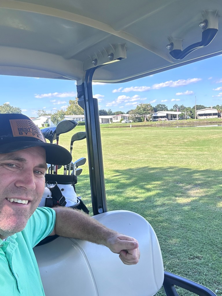 Ryan in the cart at Fairways Golf Club with the fairway and pond behind