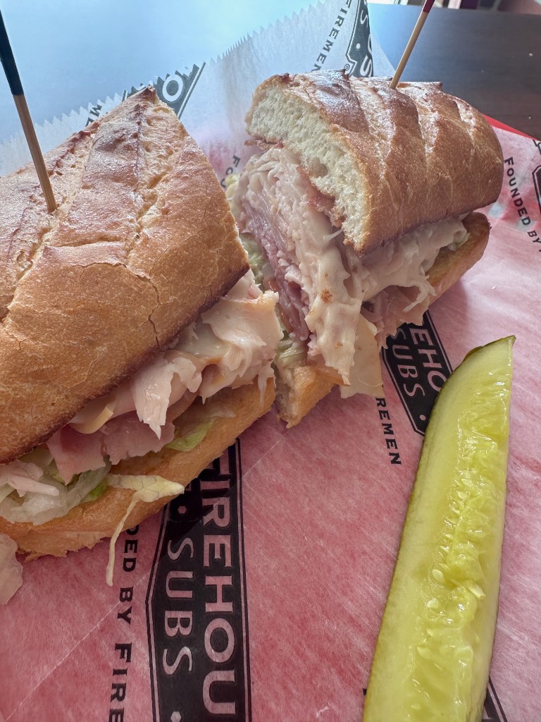 Firehouse club sub with pickle spear on branded paper