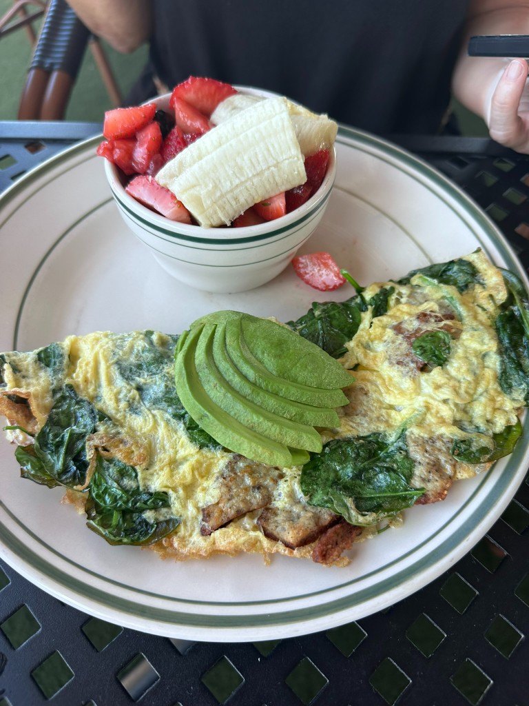Spinach and sausage omelet topped with avocado, fruit on the side