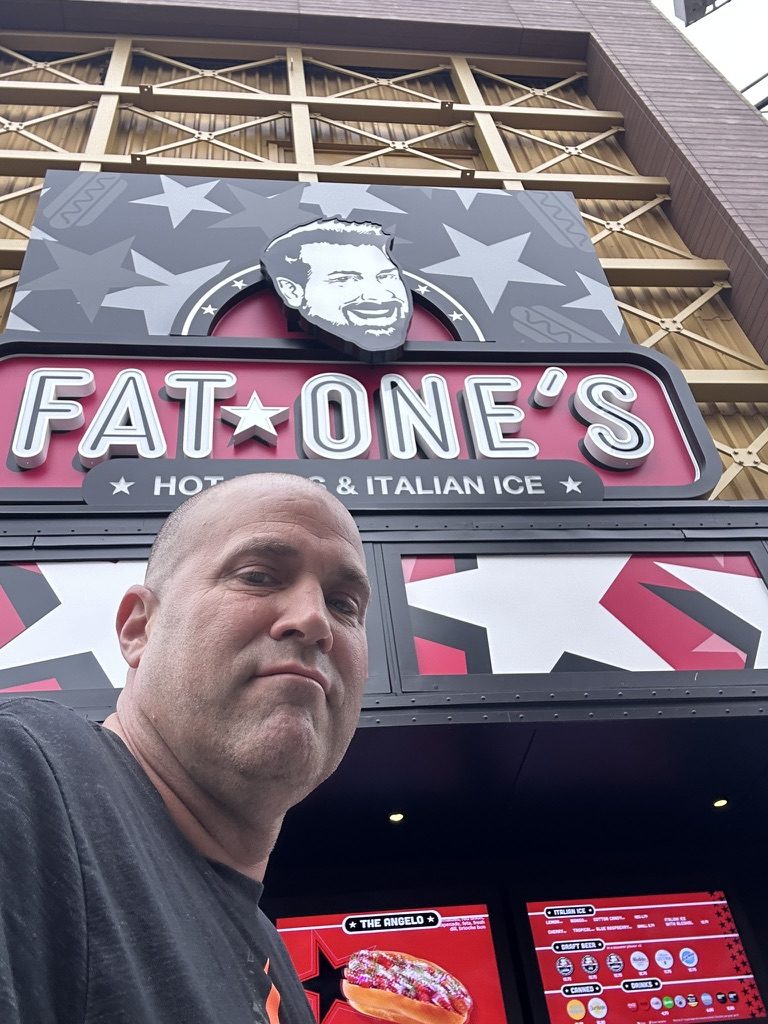 Ryan taking a selfie under the Fat One's sign with menu screens below