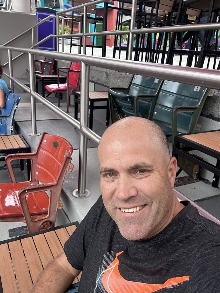 Ryan sitting among red and green stadium seats at Fat One's